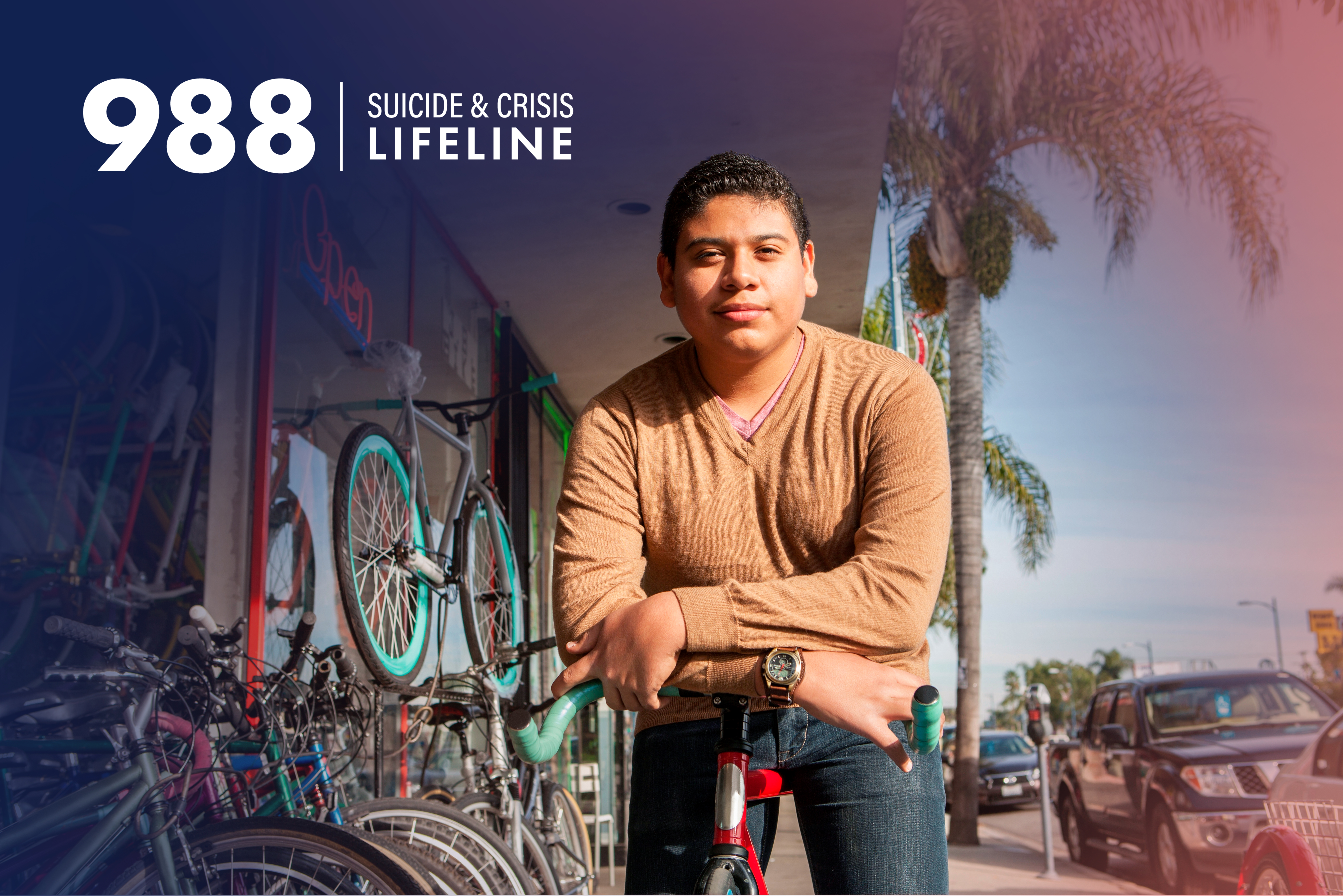 A man with a calm expression and a slight, closed-lip smile stands in front of a bike shop. Overlay text reads 988 Suicide and Crisis Lifeline.